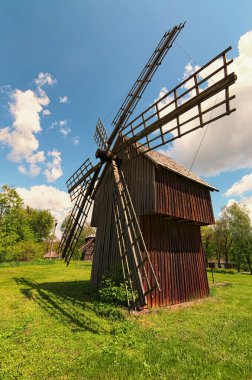 Bahar güneşli bir günde eski ahşap rüzgar değirmeninin geniş açılı manzarası. Beyaz bulutlu mavi gökyüzü arkaplanı. Antik Ukrayna 'nın tarihi binaları kavramı.