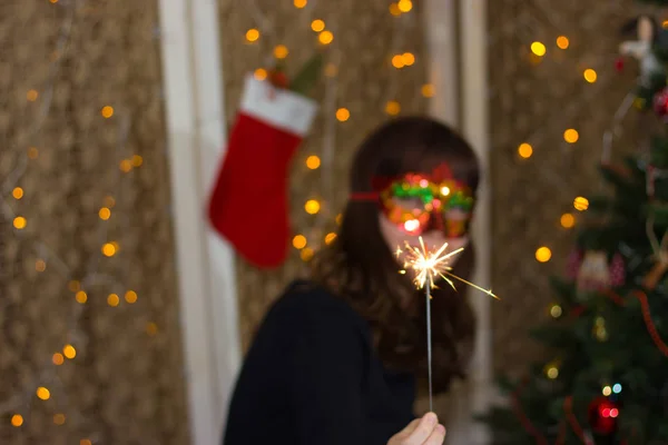 Menina em uma máscara vermelha perto de uma árvore de Natal com sparkler . — Fotografia de Stock