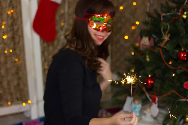 線香花火のクリスマス ツリーの近くの赤いマスクの女の子. — ストック写真