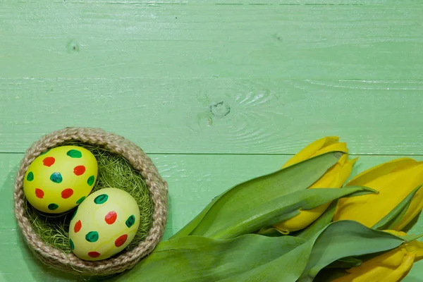 Húsvéti tojást egy kosárban. Festett tojások. Egy csokor sárga tulipán — Stock Fotó