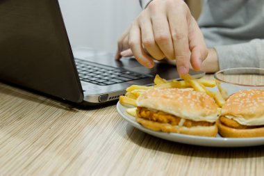 Bir adam bir bilgisayarda çalışıyor ve hızlı yemek yiyor. sağlıksız yiyecek: BÜ