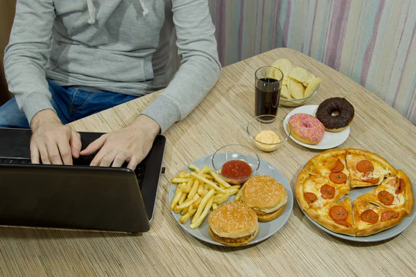 Een man werkt bij een computer en fastfood eet. ongezonde voeding: Bu — Stockfoto