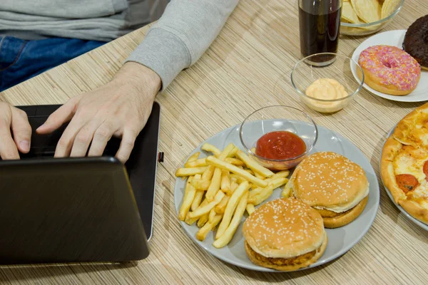 男は、コンピューターで動作し、ファーストフードを食べる。不健康な食べ物: Bu — ストック写真