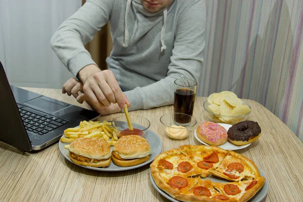 Um homem trabalha num computador e come fast food. alimentos não saudáveis: Bu — Fotografia de Stock