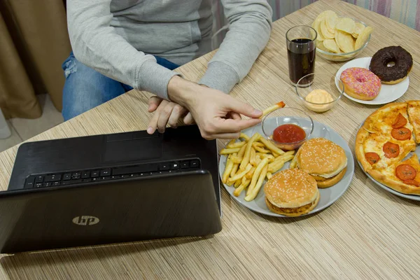 Чоловік працює за комп'ютером і їсть фастфуд. нездорова їжа: Бу — стокове фото