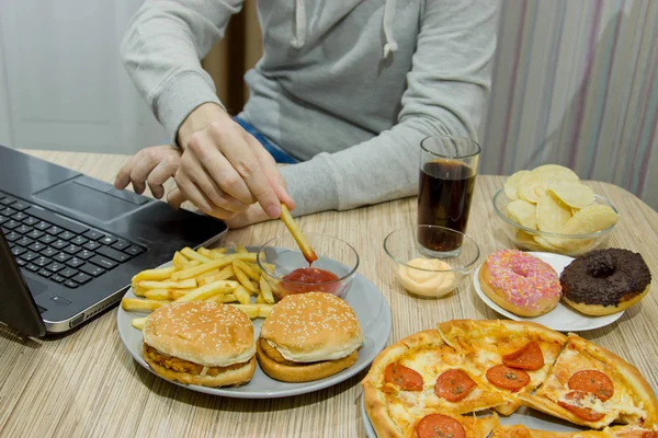Чоловік працює за комп'ютером і їсть фастфуд. нездорова їжа: Бу — стокове фото