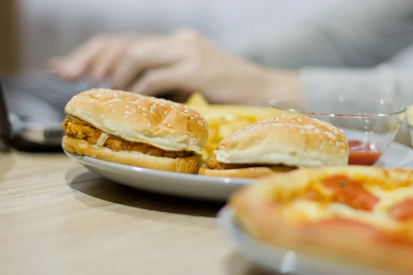 Een man werkt bij een computer en fastfood eet. ongezonde voeding: Bu — Stockfoto