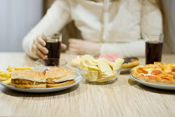 A menina está sentada à mesa e comendo fast food . — Fotografia de Stock