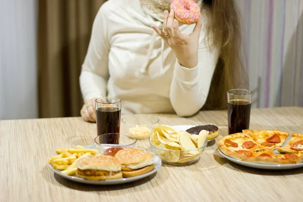 Het meisje is zittend aan tafel en eten fastfood. — Stockfoto