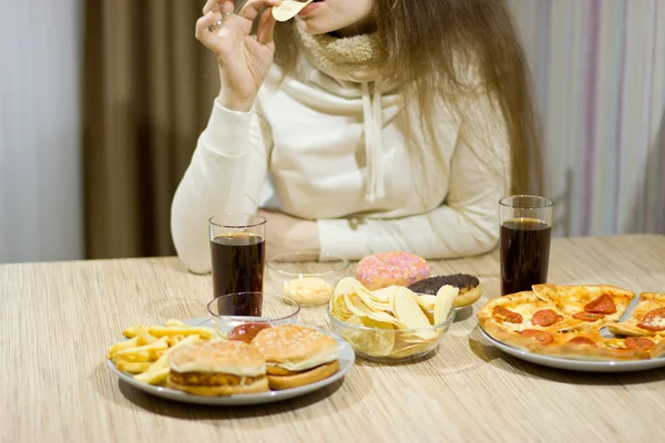 Het meisje is zittend aan tafel en eten fastfood. — Stockfoto