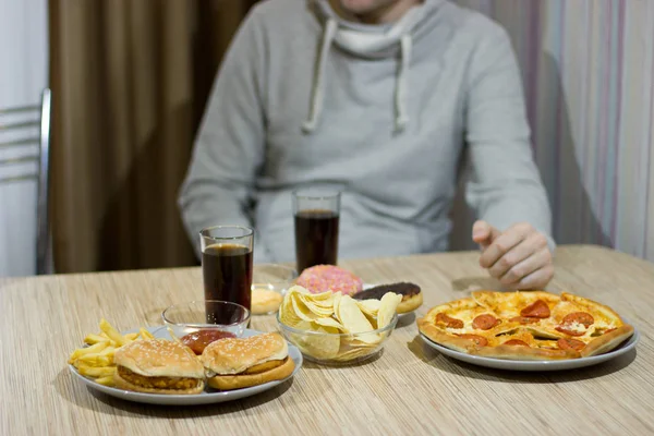 Un uomo è seduto a tavola e mangia fast food . — Foto Stock