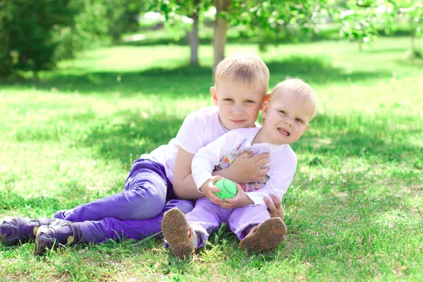 The brother hugs his younger brother in the park. Bright sunny s — Stock Photo, Image