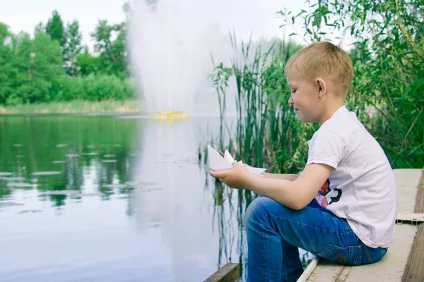 Ein Junge mit einem Papierboot am Fluss. — Stockfoto