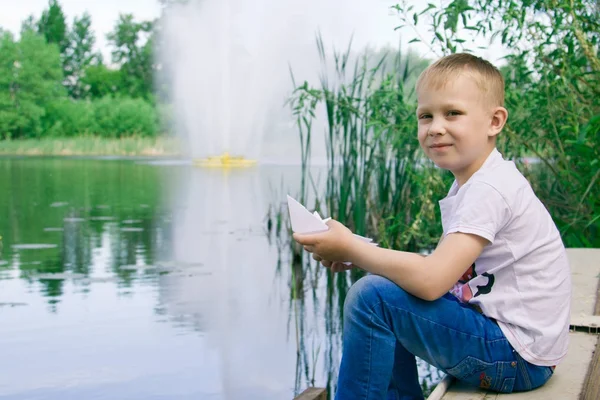 Un garçon avec un bateau en papier près de la rivière . — Photo