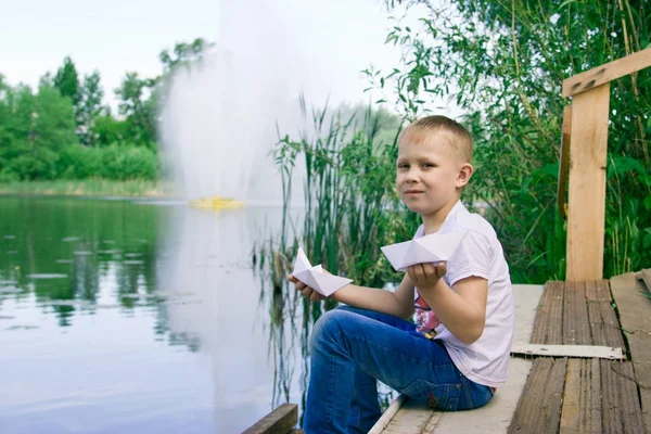 En pojke med ett papper båt vid floden. — Stockfoto