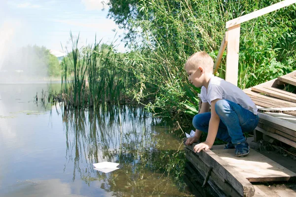 Um rapaz com um barco de papel junto ao rio . — Fotografia de Stock