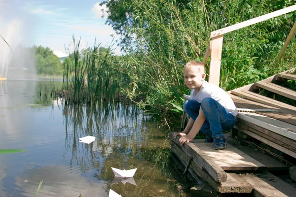 A boy with a paper boat by the river. — Stock Photo, Image