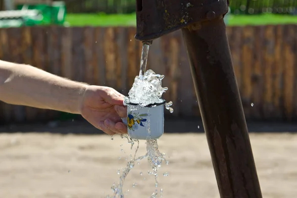 The man pours a Cup of water from the column (crane). — Stock Photo, Image