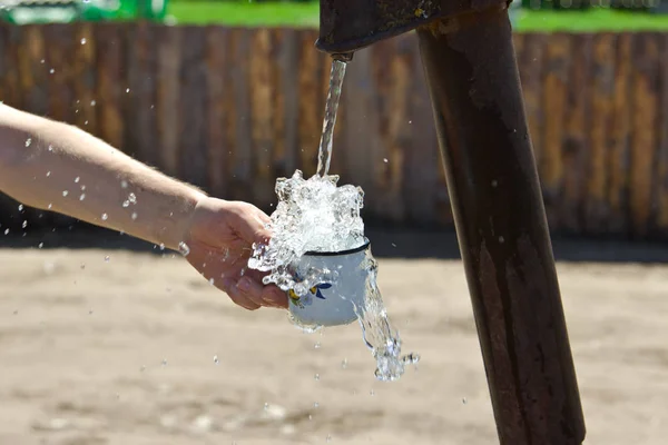 The man pours a Cup of water from the column (crane). — Stock Photo, Image