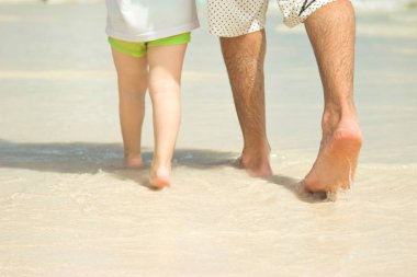 Baba ve oğul plaj boyunca yürüyor. Yakın çekim bacaklar. Beach Punta Cana, Dominik Cumhuriyeti için.