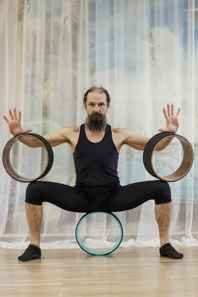 Un hombre de mediana edad se dedica al yoga con el uso de ruedas . — Foto de Stock