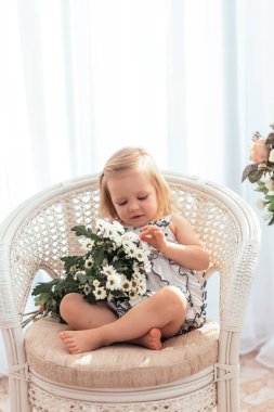 Küçük bir kız bir buket çiçekle bir sandalyede oturuyor, güneşli bir ışık..