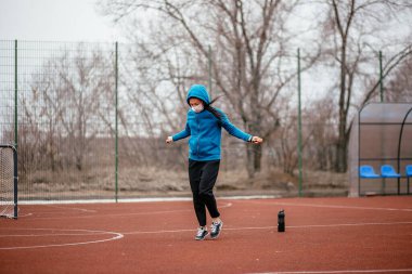 Genç bir kadın tıbbi bir maskeyle ip atlamakla meşgul. Tıbbi bir maskeyle koronavirüs enfeksiyonuna karşı koruma. Rusya 'da ilkbahar başlarında.