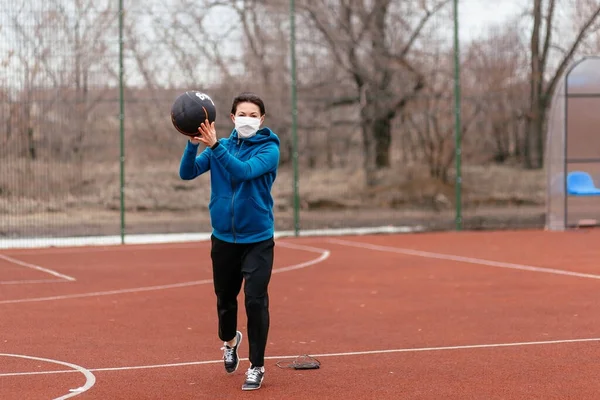 A young woman is playing sports on a sports field in a mask. Protection from coronavirus infection with a medical mask. Early spring in Russia.