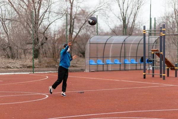 A young woman is playing sports on a sports field in a mask. Protection from coronavirus infection with a medical mask. Early spring in Russia.