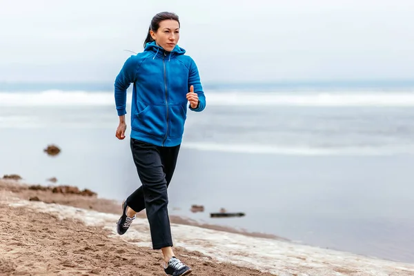 A young woman runs along the sandy Bank of the river. Early spring in Russia.