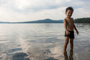 Küçük çocuk taş oynarken elinde tutan göle, suda duruyor