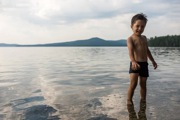 Küçük çocuk taş oynarken elinde tutan göle, suda duruyor