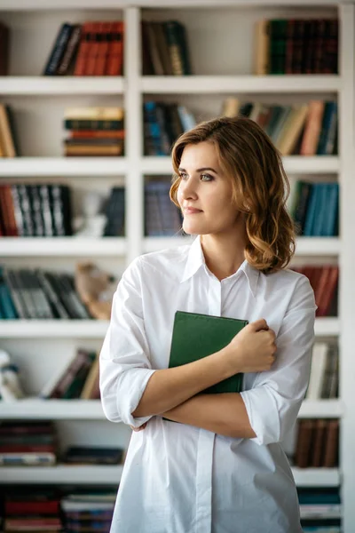 Mujer de pie con libro en la mano en la biblioteca —  Fotos de Stock