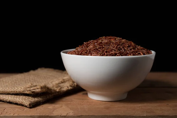 Bagas de arroz em tigela branca no fundo de madeira — Fotografia de Stock