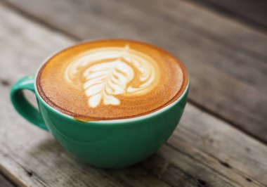 Ahşap üzerinde yeşil bir fincan cappuccino kahve