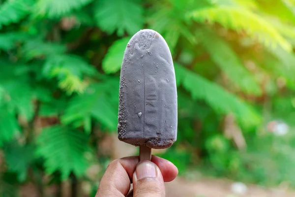 Hand with ice cream on blurred green nature background — Stock Photo, Image