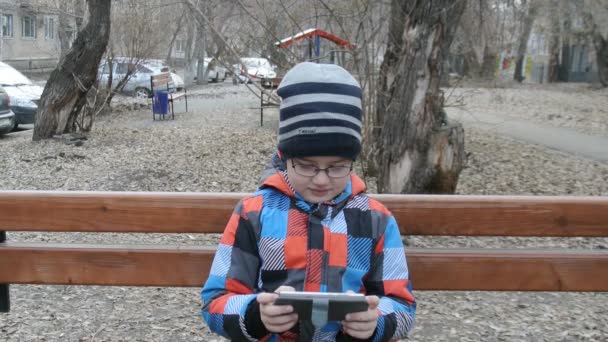 Jeune adolescent jouer à un jeu sur smartphone sur le banc à l'extérieur . — Video