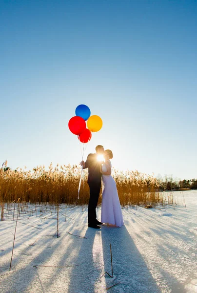 Жених и невеста идут по поверхности замёрзшего озера с воздушными шарами — стоковое фото