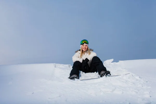Jovem mulher sentada na montanha coberta de neve com seu snowboard — Fotografia de Stock