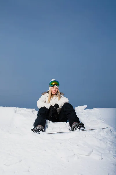 Ung kvinna sitter på snötäckta bergssidan med sin snowboard — Stockfoto