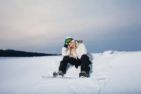 Ung kvinna sitter på snötäckta bergssidan med sin snowboard — Stockfoto