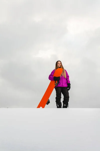 Jonge vrouw en haar oranje snowboard op een besneeuwde berghelling — Stockfoto