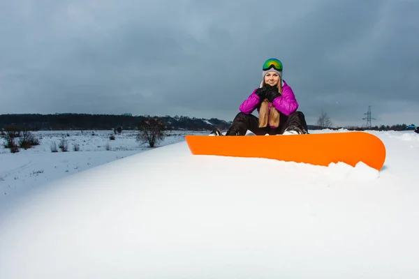 Ung sexig snowboardåkare sitter på snötäckta bergssidan — Stockfoto