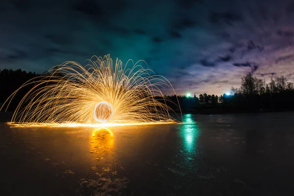 春の夜の風景の背景で凍った湖の表面に火花を燃焼の軌跡 — ストック写真