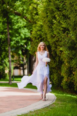 Beyaz elbiseli genç güzel gelin yaz parkta yürüyor 