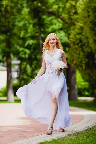 Молода красива наречена в білій сукні ходить в літньому парку — стокове фото