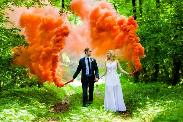 Das Brautpaar mit dem orangefarbenen Rauch vor dem Hintergrund der sommerlichen Natur — Stockfoto