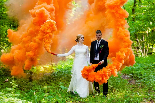 De bruid en de bruidegom met de oranje gekleurde rook op de achtergrond van zomer bos — Stockfoto