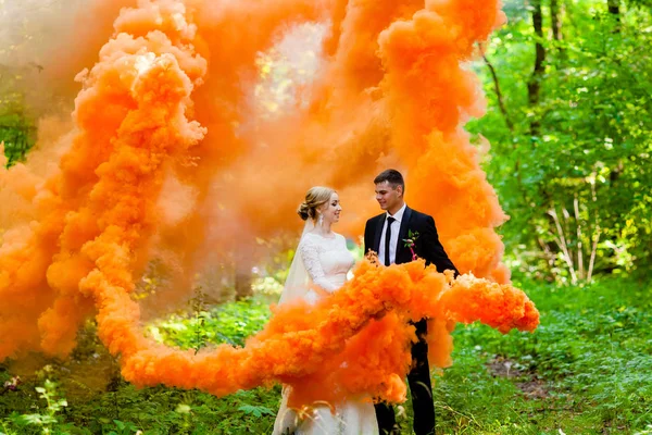 A noiva e o noivo com a fumaça cor de laranja no fundo da floresta de verão — Fotografia de Stock
