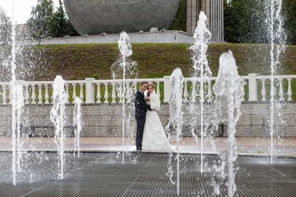 Жених и невеста рядом с фонтаном и высокими струями воды — стоковое фото